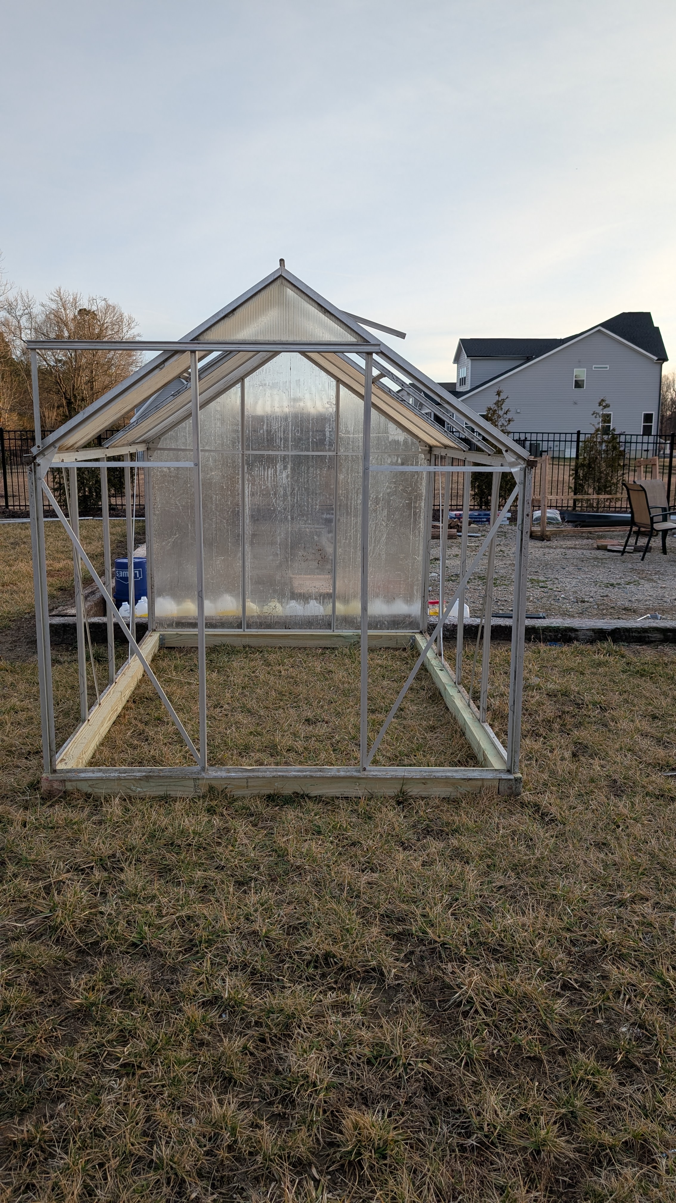 The greenhouse frame going up in the backyard — aluminum skeleton on winter grass