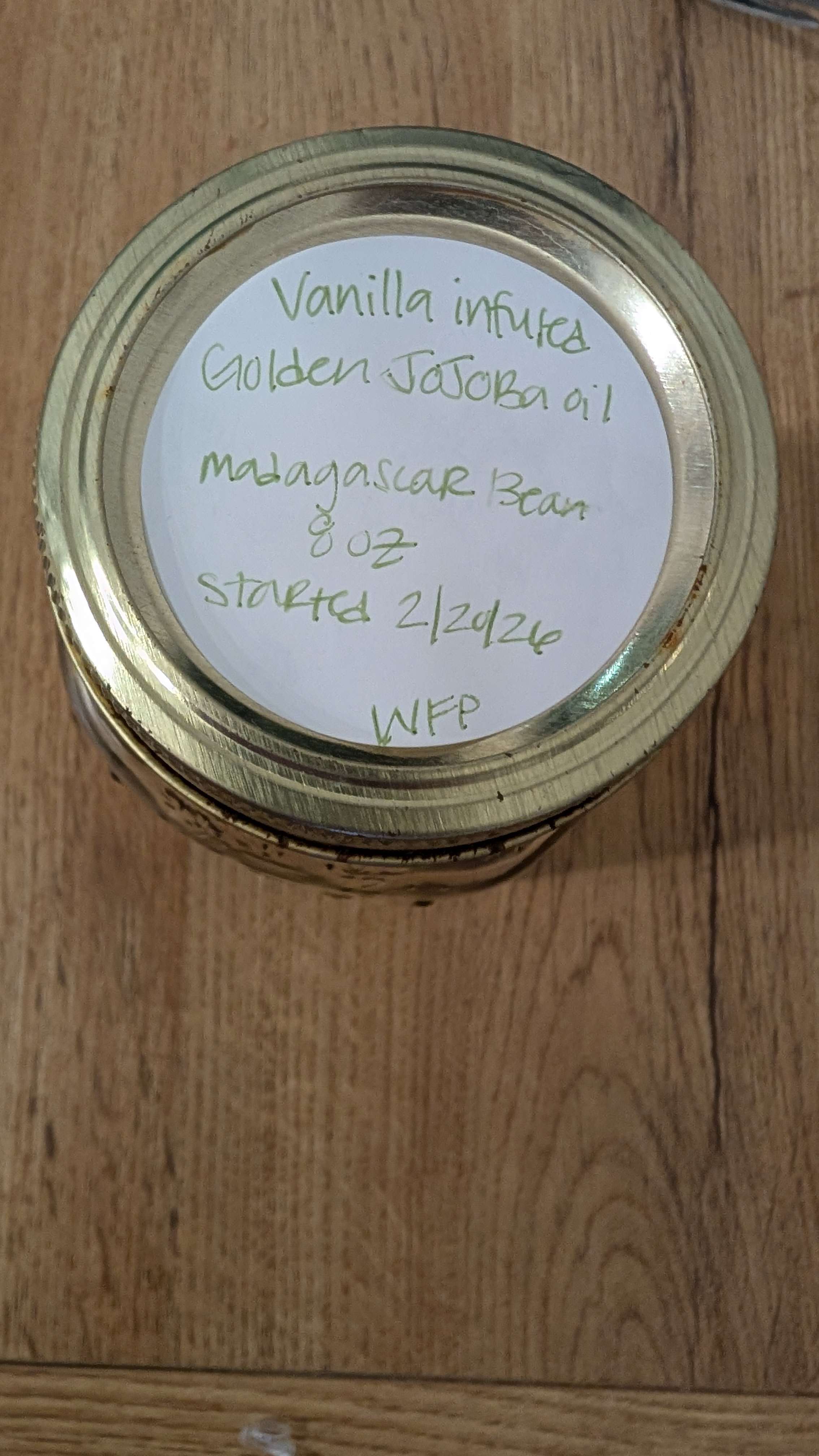 Handwritten label on a mason jar — vanilla infused golden jojoba oil, Madagascar bean, started 2/20/26